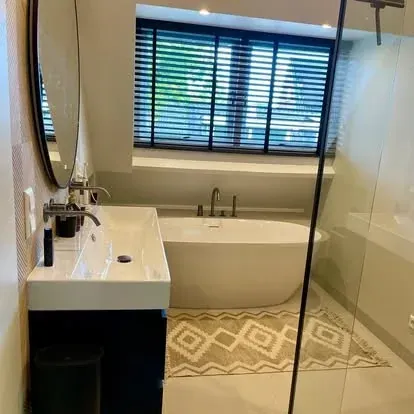 Compacte badkamer onder een schuin dak met vrijstaand bad, glazen douchewand, wastafelmeubel en ronde spiegel